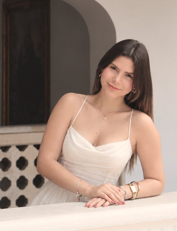 Daniela Gil de blanco, apoyada en un balcón con un arco detrás